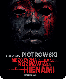 Okładka książki "Mężczyzna, który rozmawiał z hienami" autorstwa Przemysława Piotrowskiego, przedstawiająca ciemną, pękniętą maskę z czerwonymi smugami na czarnym tle.